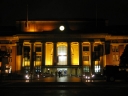 Wellington Railway Station at night. The tops of the flagpoles are shown this time, and passengers are leaving the front steps of the station.