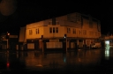 The disused building complex at Woburn shortly after midnight. The rain is visible on the road in front, particularly from the lights of the Chemist at the far right. A spot of rain appears in the top left hand corner of the frame.