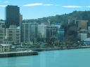 Looking out from Te Papa, further south this time. Frank Kitts Park is in the foreground. One end of the Boatshed appears on the left. On the right hand side, the reflection shows someone holding a digital camera.