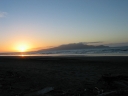 The sun sets next to Kapiti Island. The tracks in the sand in the foreground show that a car has been doing circles.