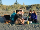Jann, Mauricio, Haydn, Paul, Snaiet, and Denise eat fish 'n' chips on Peka Peka beach. The sun is close to setting.