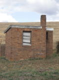 A small building just north of the barracks, looking east. The one visible window has been boarded up.