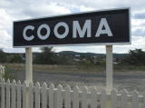 'Cooma' station board, with the town and carpark in the background.