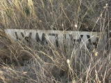 In a ditch north of the former crossing, a 'Railway' sign has been dumped.